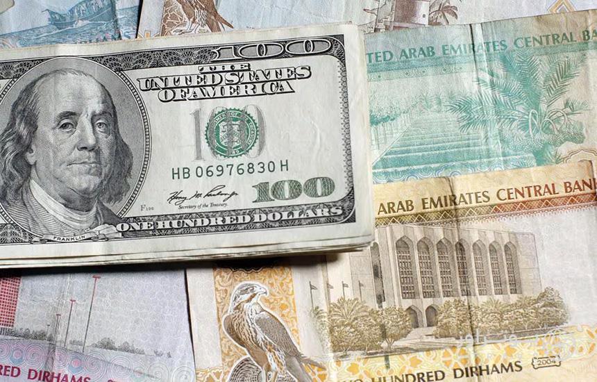تصویری از تعدادی درهم امارات که یک‌دسته دلار آمریکا روی آن‌ها در گوشه سمت چپ عکس قرار دارد.